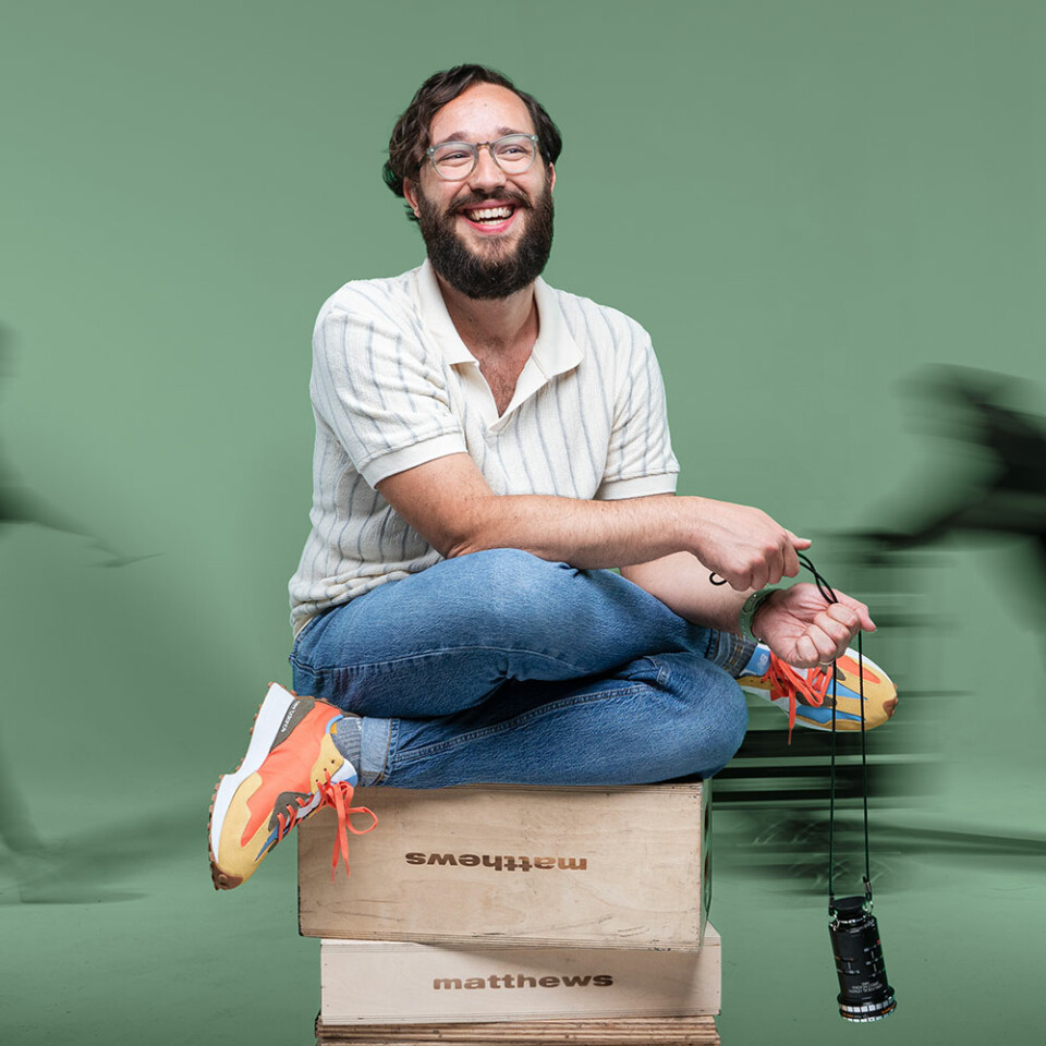 Director Joshua Henry joyfully sitting on set with a bright solid color background